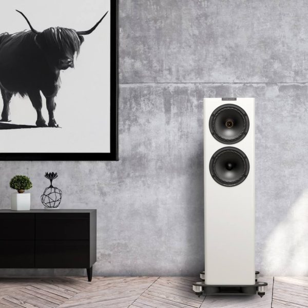 fyne audio F702SP floorstanding speaker in gloss white, Lifestyle image with highland cow picture on wall and cabinet with bonsai tree and ornament on top
