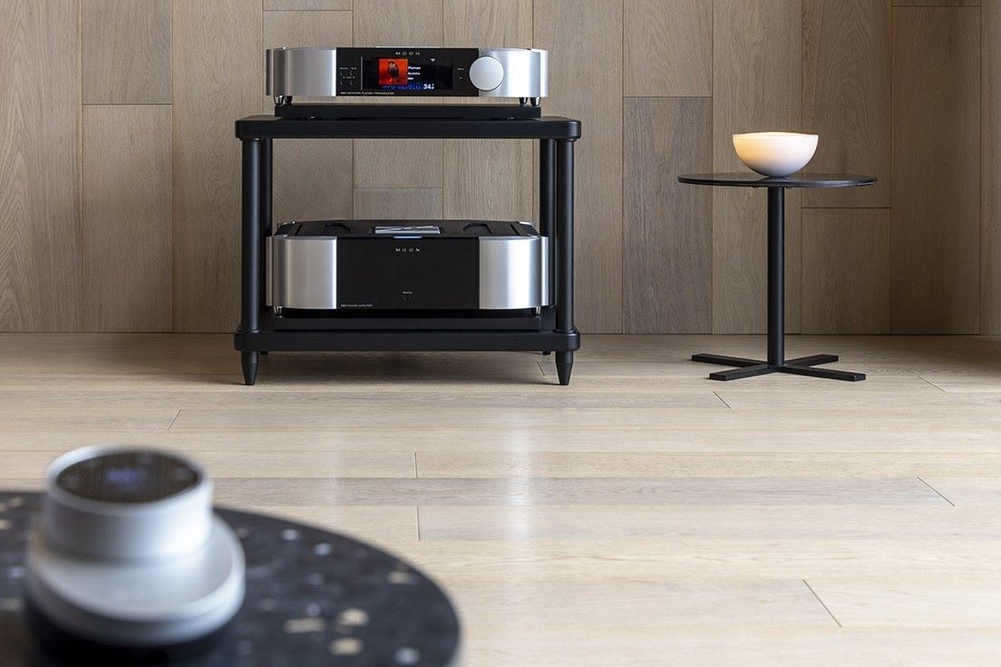 moon north collection 791 streaming preamplifier and 761 power amplifier lifestyle image with table to the side and remote control in foreground