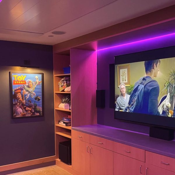 Robin House Cinema room with sony 85 inch television and surround sound speaker system with purple led lighting around the screen and ceiling. disney posters on the wall of inside out 2 and toy story movies