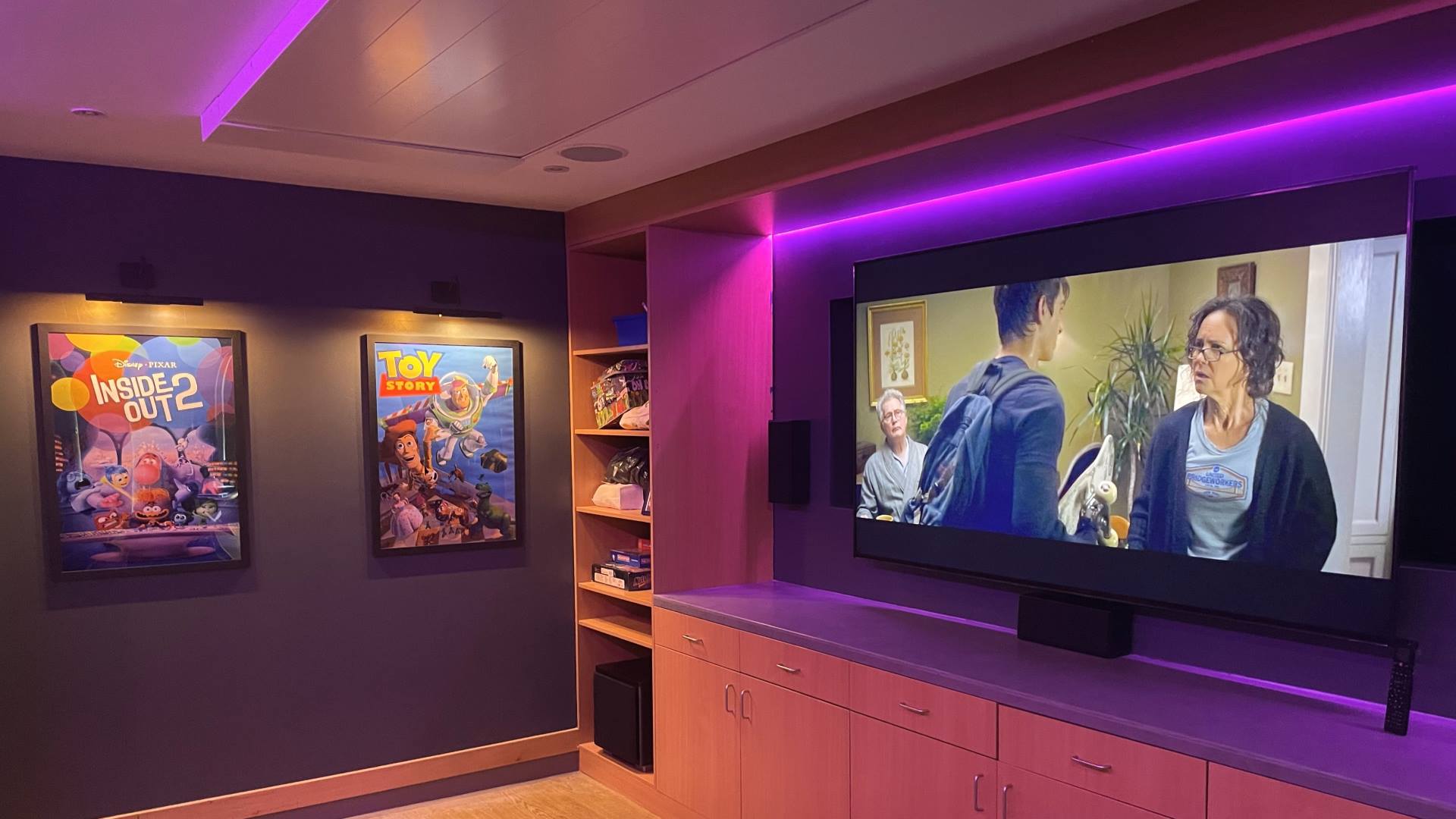 Robin House Cinema room with sony 85 inch television and surround sound speaker system with purple led lighting around the screen and ceiling. disney posters on the wall of inside out 2 and toy story movies