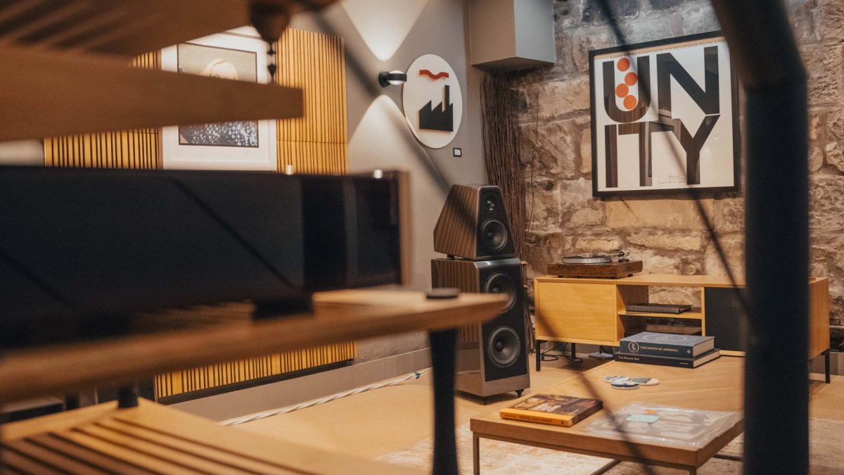 Wilson Audio WATT/Puppy high-end audio floorstanding speakers in demonstration room viewed through iron hand rail and quadraspire SVT equipment rack with larry young unity album cover and factory records art work on wall