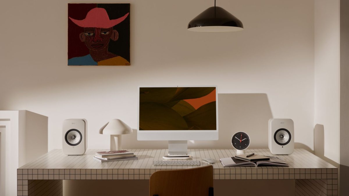 KEF LSX ii LT Wireless Speakers on desk with imac computer screen, keyboard and mouse with lampshade hanging down and artwork on the wall, lifestyle audio from loud and clear glasgow, scotland, uk