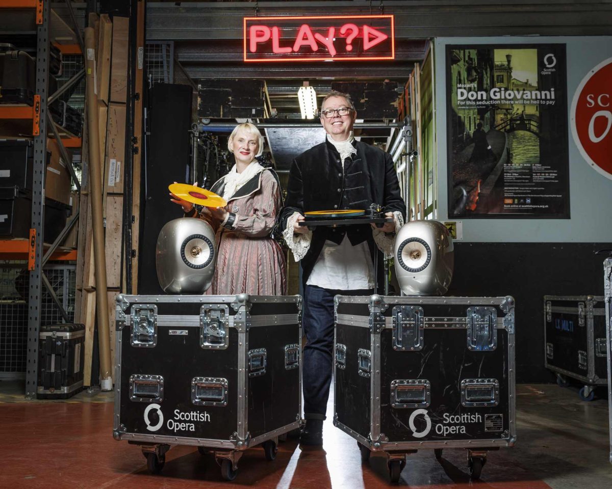 allan from loud and clear and isla from scottish opera dressed up in costume for a promo picture with kef ls luxe speakers on flight cases and allan holding a rega planar turntable and isla holding a vinyl record